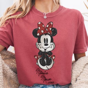 A person wearing a red t-shirt with a Minnie Mouse graphic printed on it.