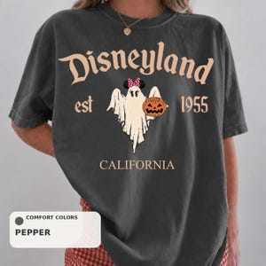 A person wearing a black t-shirt with a graphic design featuring a ghost, a pumpkin, and the text "Disneyland est 1955" and "California".