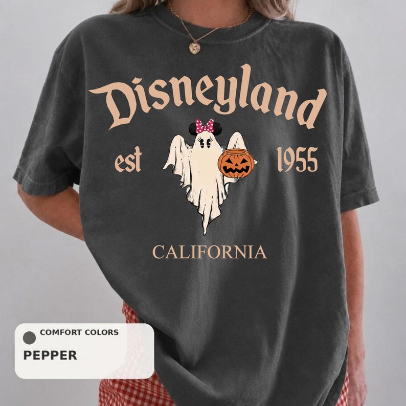 A person wearing a black t-shirt with a graphic design featuring a ghost, a pumpkin, and the text "Disneyland est 1955" and "California".