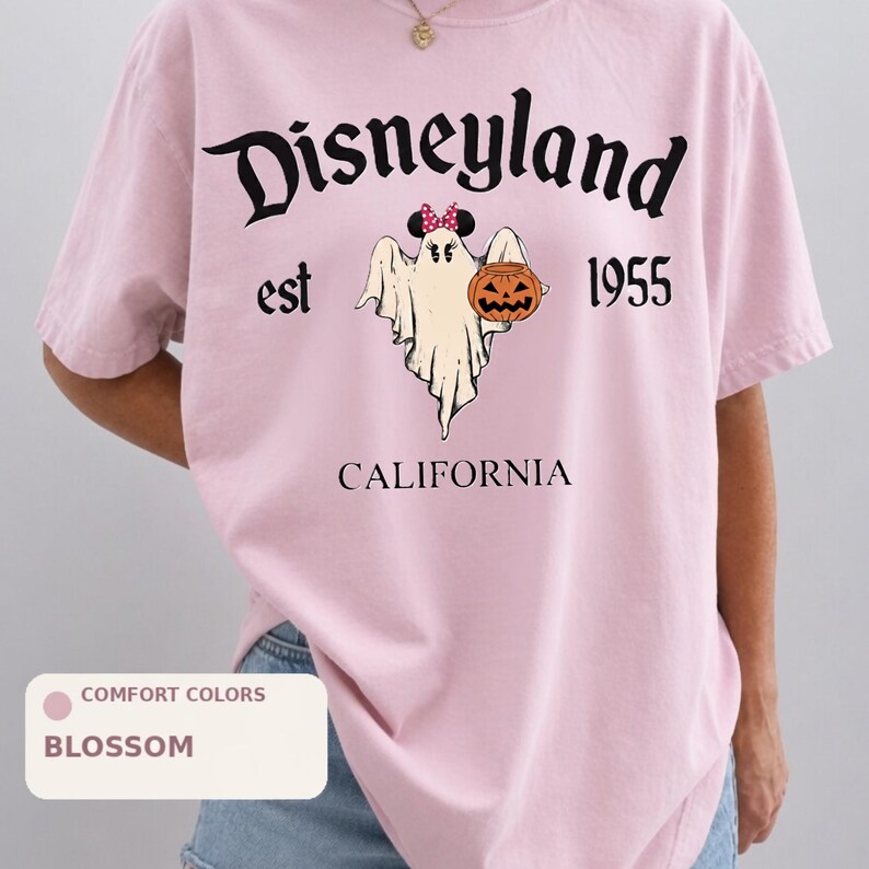 A person wearing a pink t-shirt with a graphic design of a ghost and a pumpkin, along with the text "Disneyland est 1955" and "California".