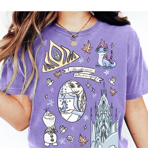A person wearing a purple t-shirt with various cartoon-style illustrations and characters, including a princess, a castle, and other whimsical elements.