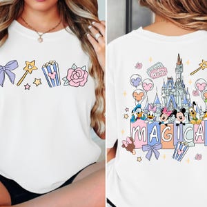 A white t-shirt with a Disney-themed design, featuring characters from the Disney film series and the word "MAGICA" prominently displayed.
