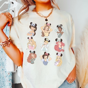 A person wearing a white t-shirt with a graphic of various Disney princesses.