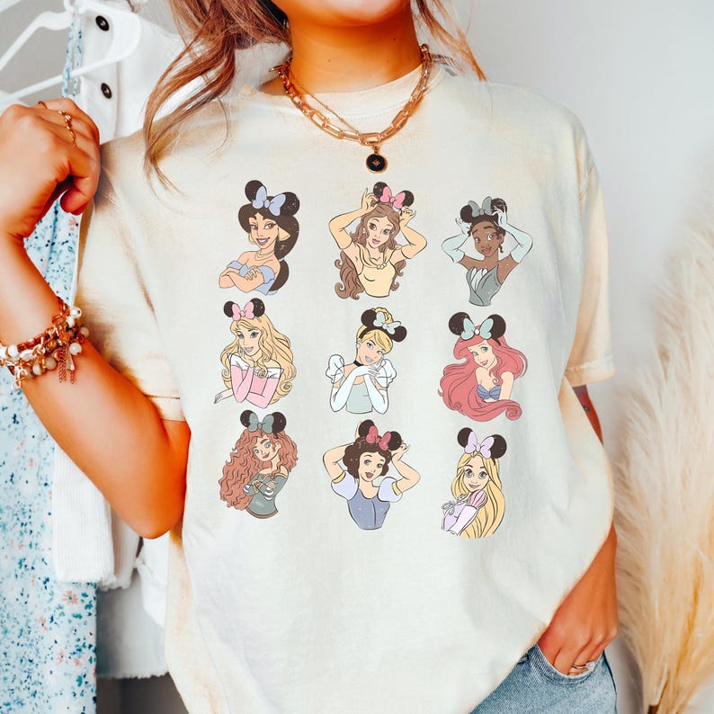 A person wearing a white t-shirt with a graphic of various Disney princesses.