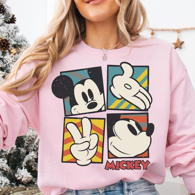 A woman wearing a pink sweatshirt with a graphic of Mickey Mouse and the word "MICKEY" printed on it.
