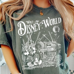 A person wearing a green t-shirt with a graphic design depicting various Disney characters and landmarks, including Mickey Mouse and the Eiffel Tower.
