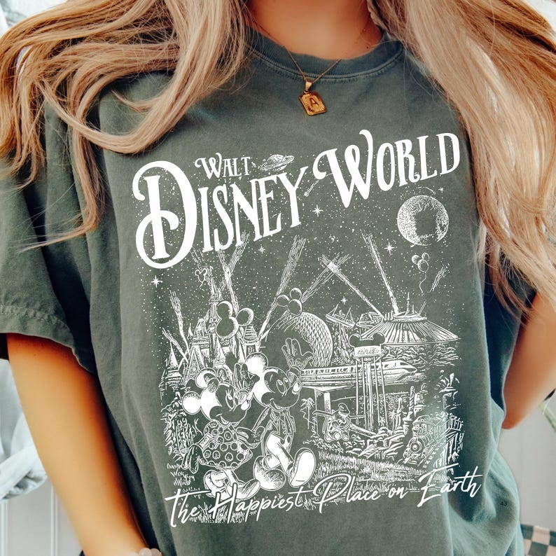 A person wearing a green t-shirt with a graphic design depicting various Disney characters and landmarks, including Mickey Mouse and the Eiffel Tower.