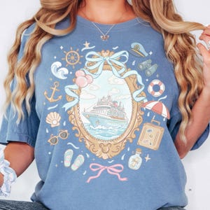 A woman wearing a blue t-shirt with a graphic design featuring a ship, various nautical elements, and a bow.