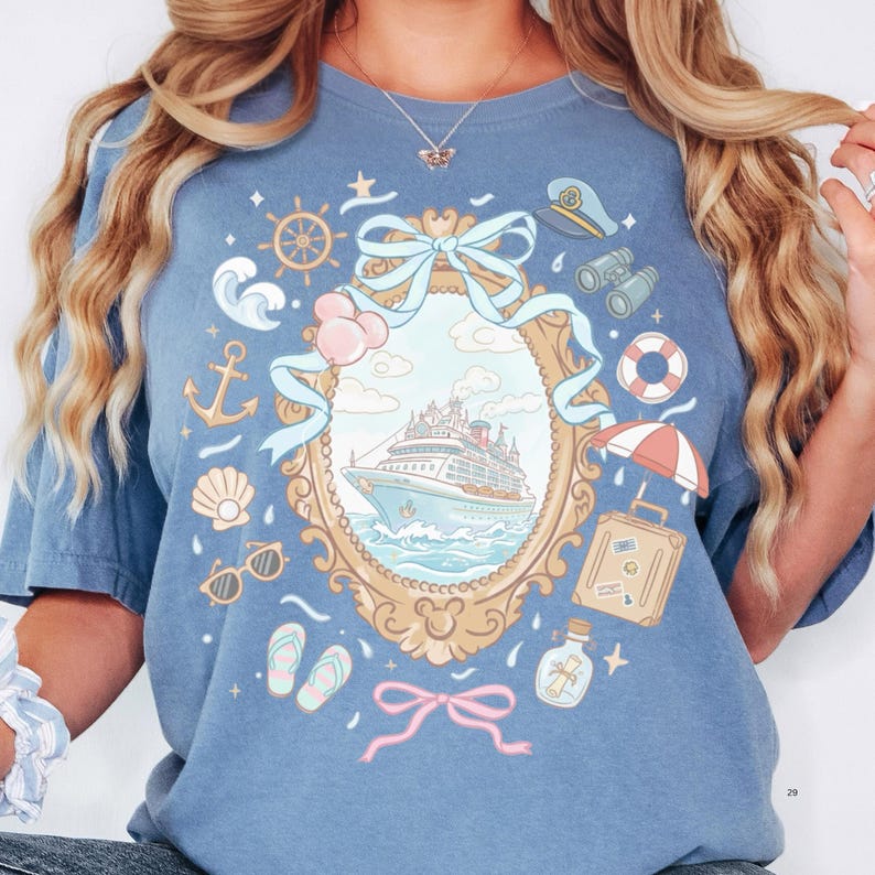 A woman wearing a blue t-shirt with a graphic design featuring a ship, various nautical elements, and a bow.