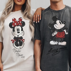 A woman and a man standing next to each other, both wearing t-shirts with Mickey Mouse designs.