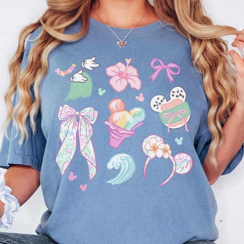 A woman wearing a blue t-shirt with various Disney-themed illustrations, including Mickey Mouse, flowers, and other whimsical designs.
