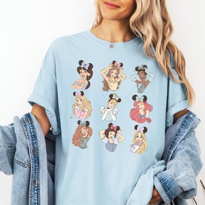 A woman wearing a light blue t-shirt with a graphic of various Disney princesses.