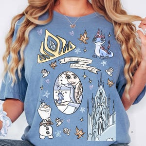A woman wearing a blue t-shirt with various cartoon-style illustrations and characters, including a princess, a dragon, and a castle.