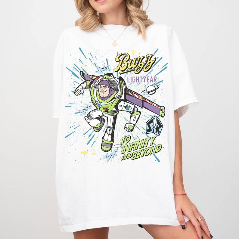 A white t-shirt with a colorful graphic of a character from the Toy Story franchise, specifically Buzz Lightyear, flying through space with a starburst effect.