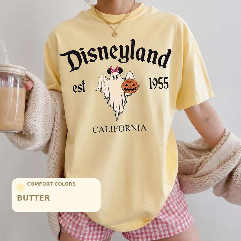 A person wearing a yellow t-shirt with a graphic of a ghost and a pumpkin, along with the text "Disneyland est 1955" and "California".