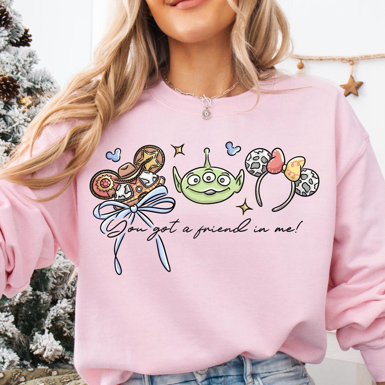 A woman wearing a pink sweatshirt with a graphic design featuring a green alien character and various Disney-themed accessories.