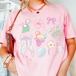 A person wearing a pink t-shirt with various Disney-themed illustrations, including Mickey Mouse, flowers, and other whimsical designs.