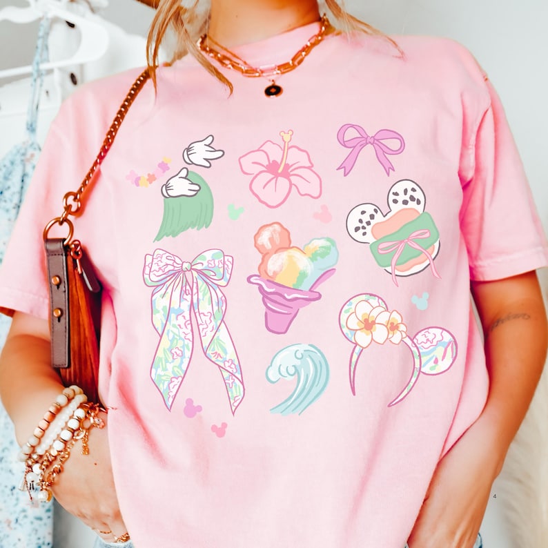 A person wearing a pink t-shirt with various Disney-themed illustrations, including Mickey Mouse, flowers, and other whimsical designs.