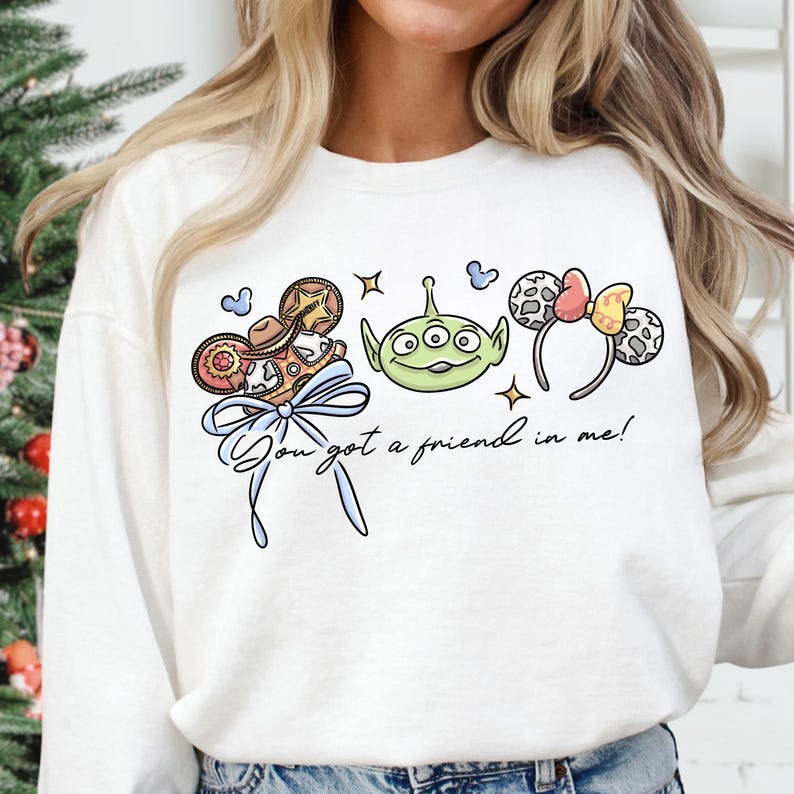 A woman wearing a white sweatshirt with a graphic design featuring a green alien character and various Disney-themed elements.