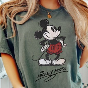 A person wearing a green t-shirt with a Mickey Mouse graphic printed on it.