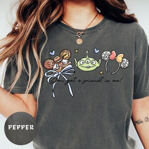 A person wearing a gray t-shirt with a graphic design featuring a green alien character and various other cartoon-like elements.