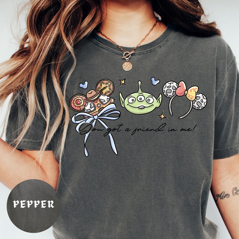 A person wearing a gray t-shirt with a graphic design featuring a green alien character and various other cartoon-like elements.