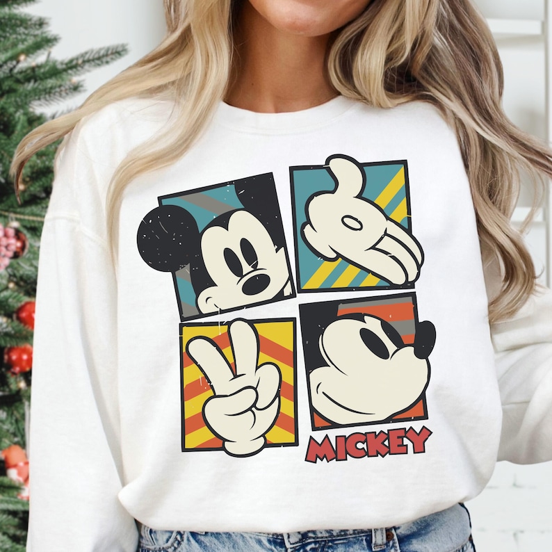A woman wearing a white sweater with a graphic design featuring the four iconic cartoon characters from the Disney movie Mickey Mouse.