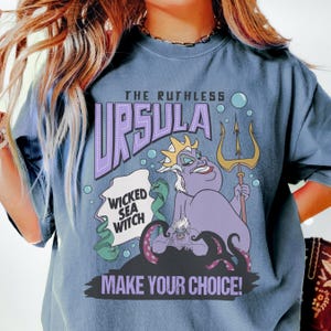 A person wearing a blue t-shirt with a graphic design featuring the character Ursula from the Disney film "The Little Mermaid".