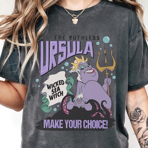 A person wearing a black t-shirt with a graphic design featuring the character Ursula from the Disney animated film "The Little Mermaid". The design includes Ursula holding a trident and the text "Wicked Sea Witch" and "Make Your Choice!"