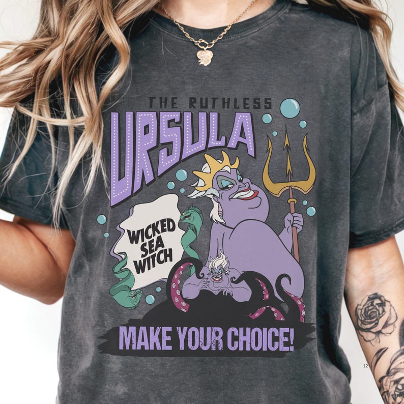 A person wearing a black t-shirt with a graphic design featuring the character Ursula from the Disney animated film "The Little Mermaid". The design includes Ursula holding a trident and the text "Wicked Sea Witch" and "Make Your Choice!"