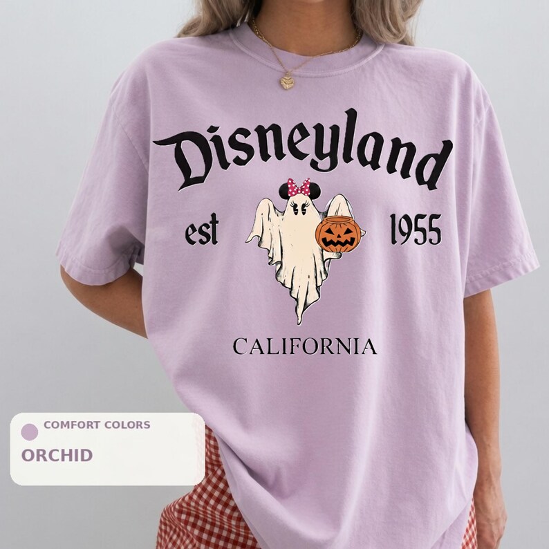 A person wearing a purple t-shirt with a graphic of a ghost and a pumpkin, along with the text "Disneyland est 1955" and "California".