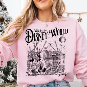 A woman wearing a pink sweatshirt with a graphic design featuring Disney characters and the text "Walt Disney World" printed on it.