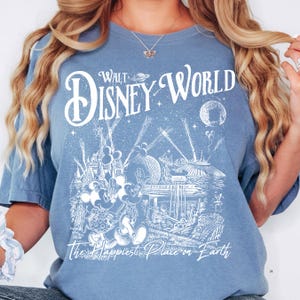 A woman wearing a blue t-shirt with a graphic design depicting Disney characters and landmarks, including Mickey Mouse and the Eiffel Tower.