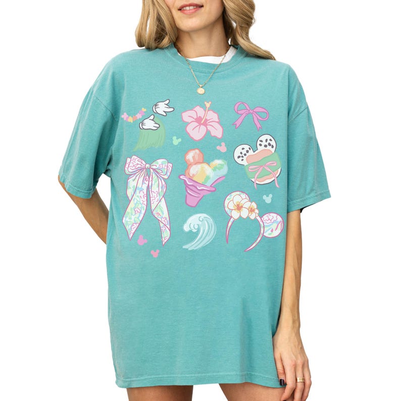 A woman wearing a turquoise t-shirt with various cartoon-style illustrations and designs, including Mickey Mouse and other whimsical elements.