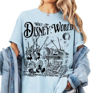 A woman wearing a light blue t-shirt with a graphic design depicting various Disney characters and landmarks, along with the text "Walt Disney World" and "The Happiest Place on Earth".