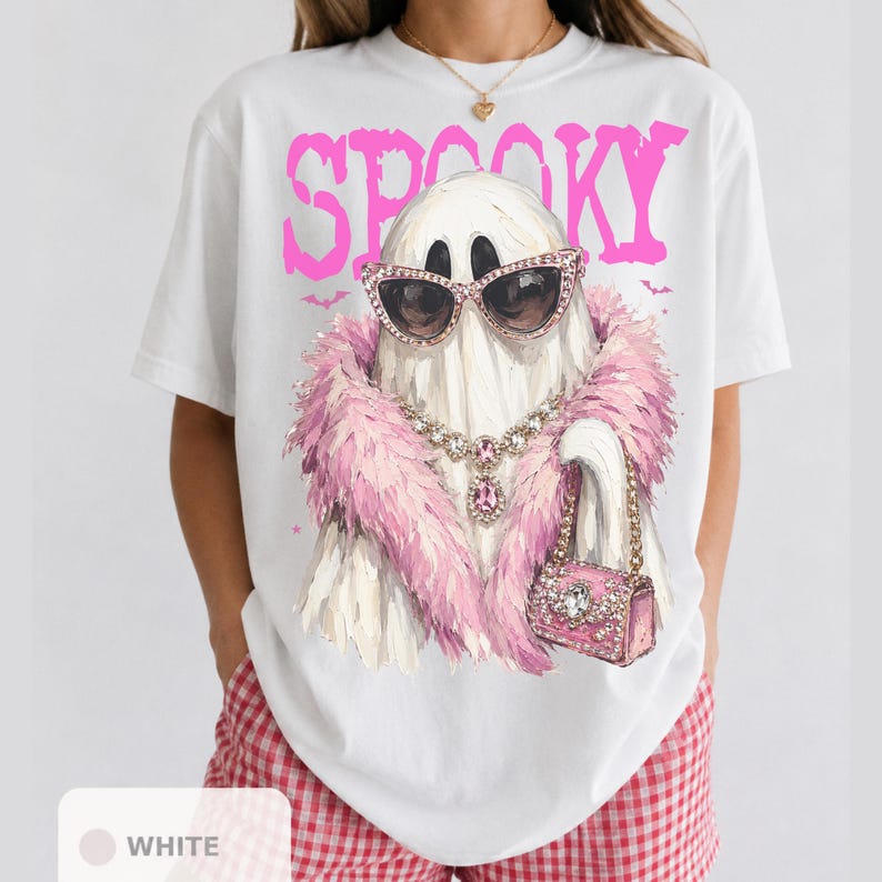 A white t-shirt with a graphic design of a ghost wearing sunglasses, a pink feathered scarf, and holding a pink purse.