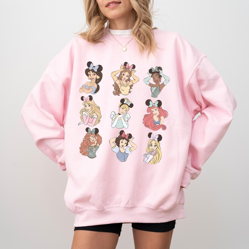 A woman wearing a pink sweatshirt with a graphic of various Disney princesses.