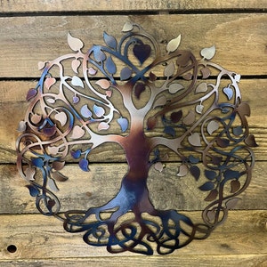 Op de afbeelding: Een metalen wanddecoratie in de vorm van een levensboom met ingewikkelde takken en wortels. De boom is geschilderd in tinten blauw, paars en bruin, wat een verloop cre&euml;ert.