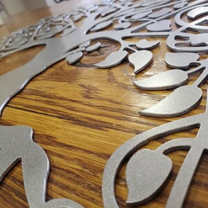 Op de afbeelding: Een zilveren metalen boomwanddecoratie met ingewikkelde takken en bladeren. De boom is gemonteerd op een houten oppervlak.