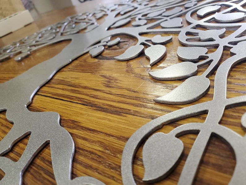 Op de afbeelding: Een zilveren metalen boomwanddecoratie met ingewikkelde takken en bladeren. De boom is gemonteerd op een houten oppervlak.