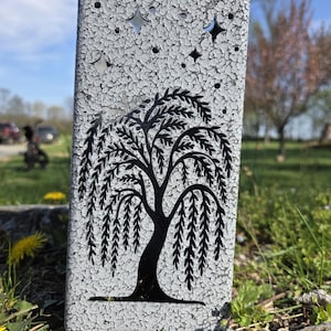 May include: A rectangular metal panel with a textured, crackled white and gray finish. The panel features a laser-cut design of a weeping willow tree in the center, with various star shapes cut out along the top portion of the surface.