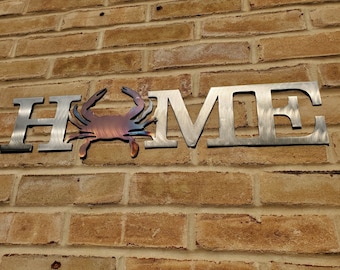 May include: Metal wall art with the word "HOME" in silver with a rusty brown crab in the center of the word.