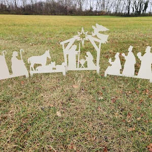 May include: White metal silhouette cutouts of a nativity scene with a star, angel, donkey, sheep, and figures of Mary, Joseph, and the three wise men.