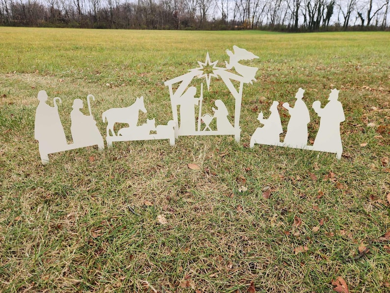 May include: White metal silhouette cutouts of a nativity scene with a star, angel, donkey, sheep, and figures of Mary, Joseph, and the three wise men.