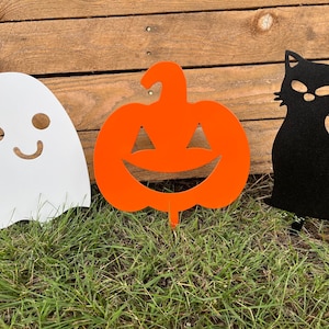 May include: Three Halloween yard decorations: a white ghost with a smiling face, an orange pumpkin with a jack-o'-lantern face, and a black cat with a curled tail.