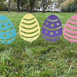 May include: Four colorful Easter egg cutouts in a row on a grassy lawn. The eggs are blue, yellow, purple, and pink. Each egg has a different pattern.