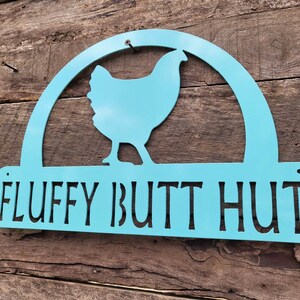 May include: A turquoise metal sign with a silhouette of a chicken and the text "FLUFFY BUTT HUT".