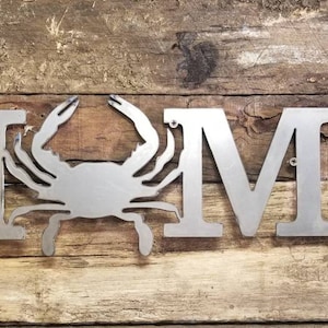 May include: Metal home sign with a crab silhouette in the center. The sign reads "HOME" in large, bold letters.