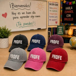 May include: Six baseball caps in various colors, including black, navy, gray, pink, and red. Each cap has the word "PROFE" embroidered in white block letters on the front. The caps are displayed on a wooden surface.