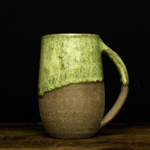 Peut inclure: Une tasse en céramique avec un glaçage vert et brun. La tasse a un corps arrondi et une anse.
